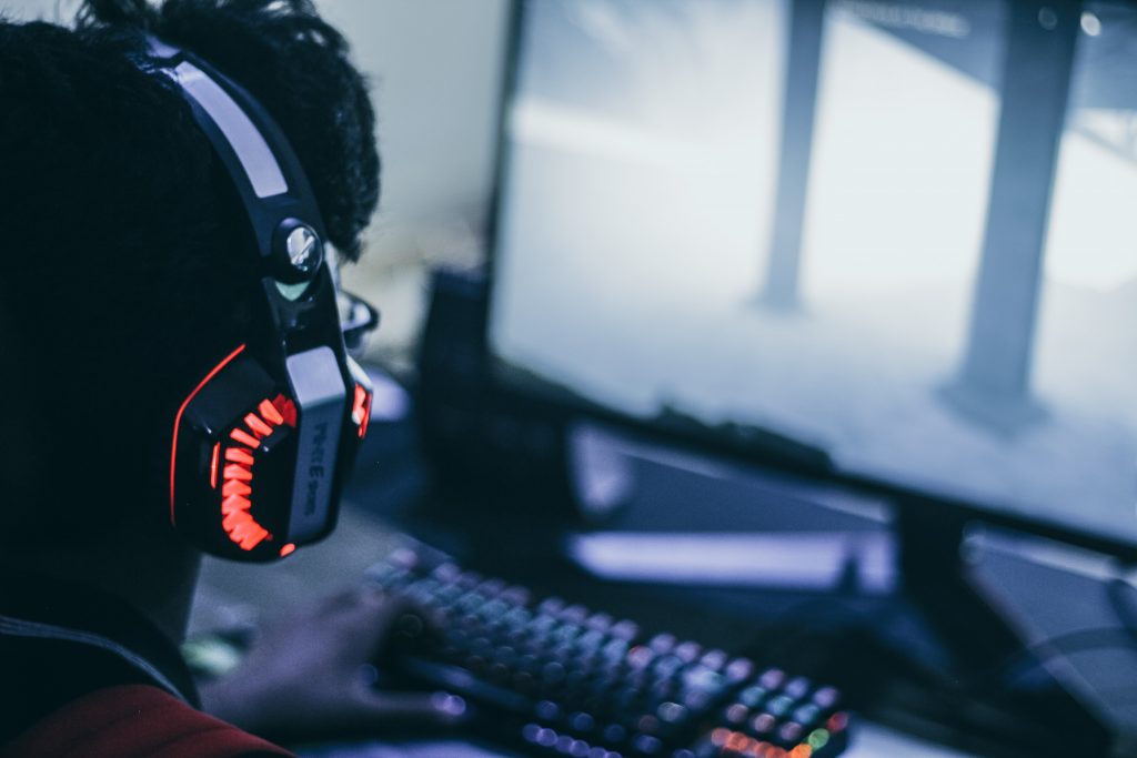 A man wearing an Xbox headset while playing a video game on their PC.